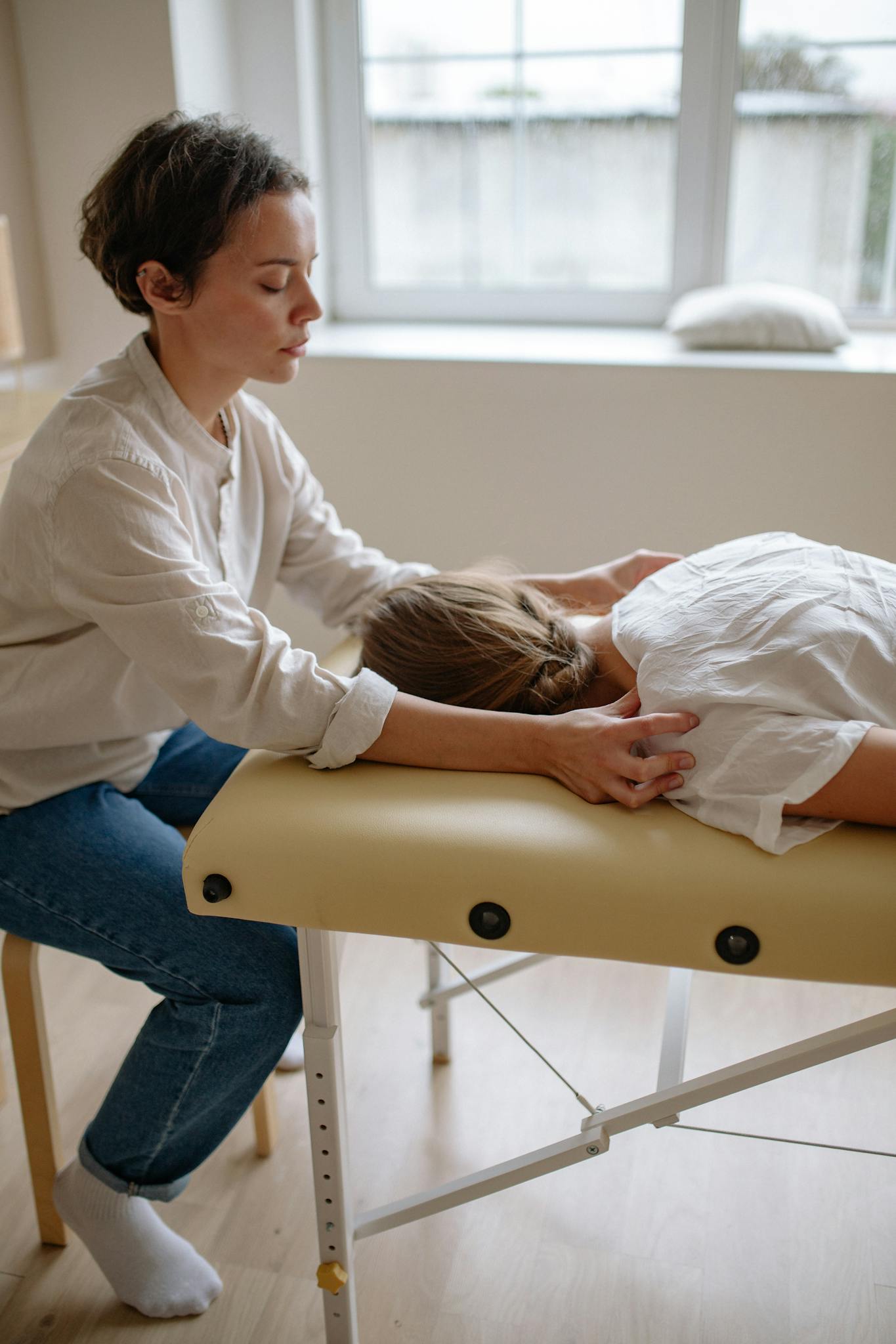 A therapist performing a massage on a woman lying on a massage table indoors.