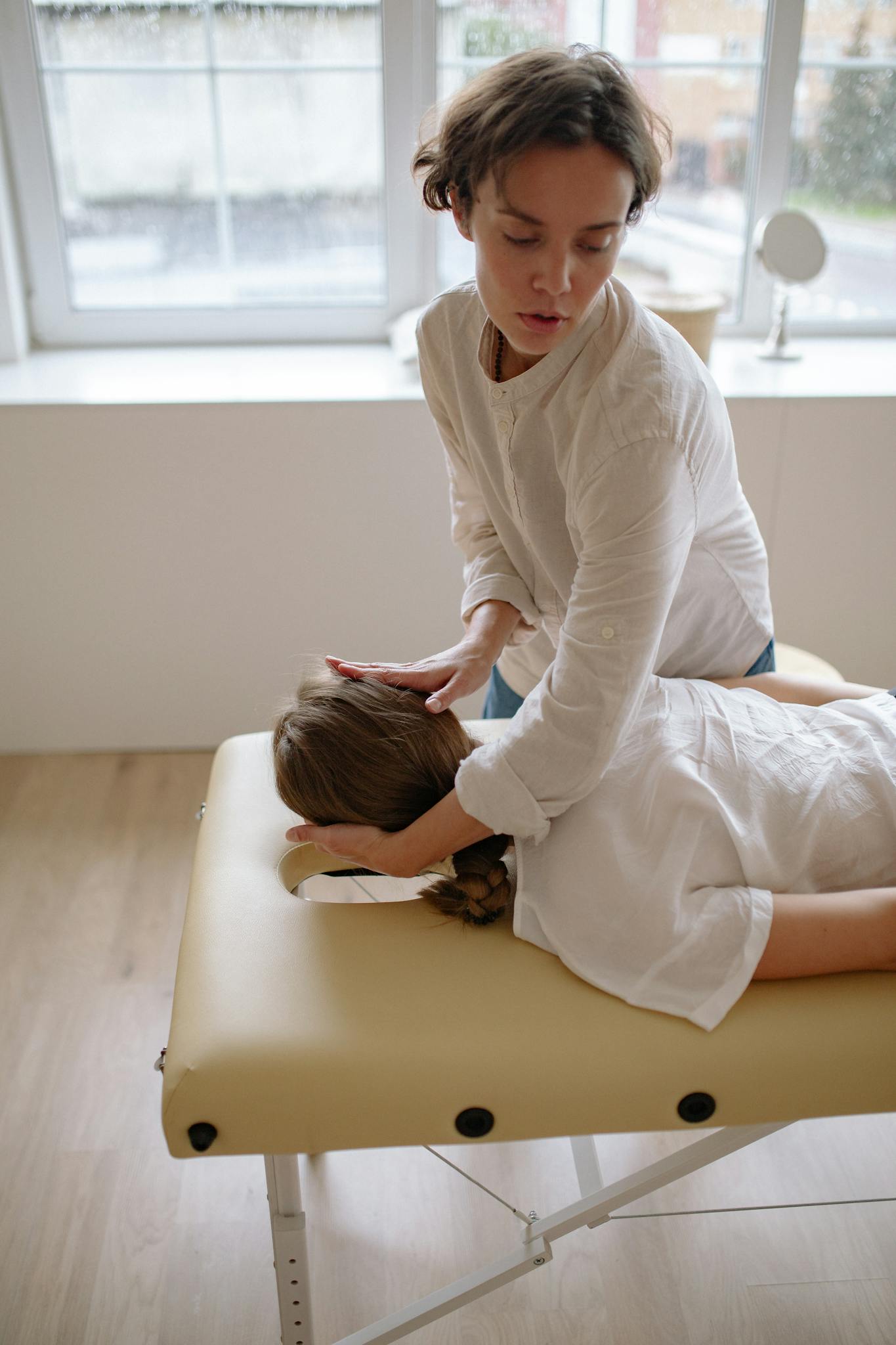 Massage therapist performing head massage on client on table in a serene indoor setting.